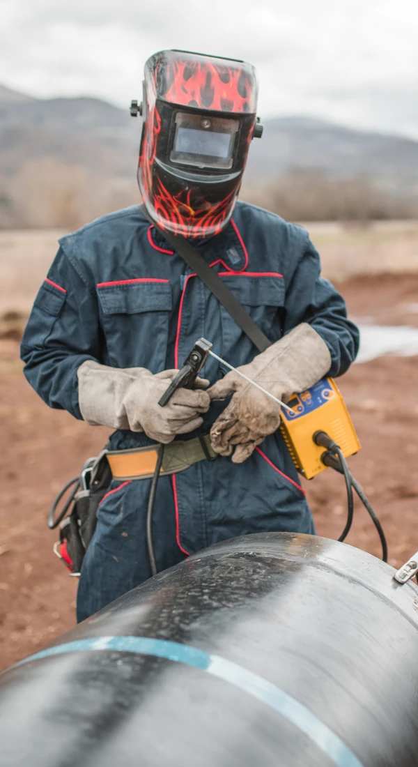 Welder working on metal pipe outdoors.